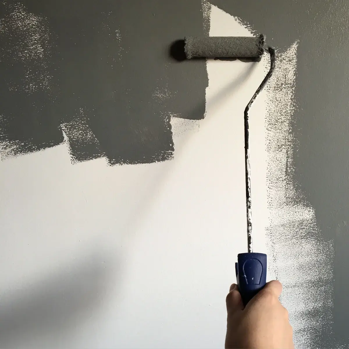 A hand holding a paint roller against a partially painted gray wall.